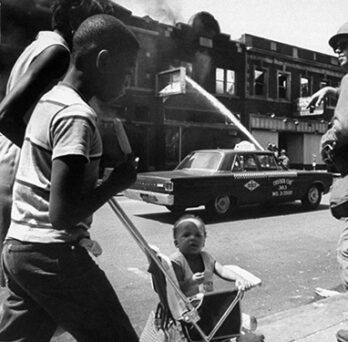 Black-and-white photo of a child in a stroller on a city street near an armed National Guard soldier. Detroit, July 1967. Source: Lee Balterman—Time & Life Pictures/Getty Images 