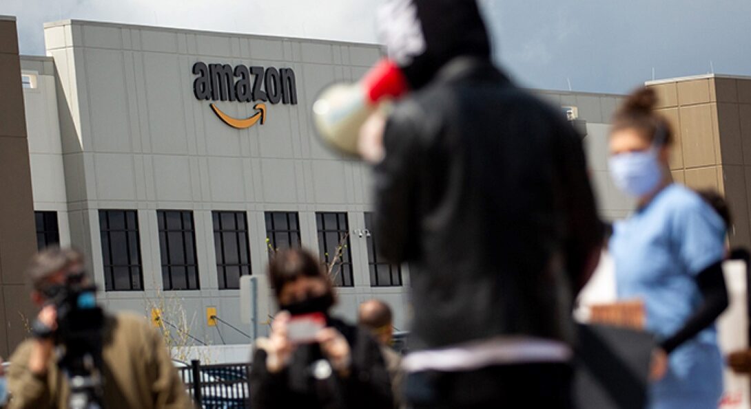 People stand outside an amazon warehouse building with megaphones.