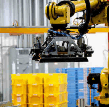 Robotic arm operating in warehouse, stacking yellow crates on pallets in industrial setting with workers nearby. 
