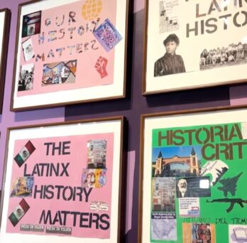 A gallery wall displays framed posters and student artwork focused on Latino and Latinx history and social justice. The posters include messages such as “Our History Matters,” “Latinx History Matters,” and “We Deserve Credit Too,” along with collages of historical figures, cultural symbols, and images related to civil rights movements. The colorful display is mounted on a purple wall with a mural partially visible on the left. 