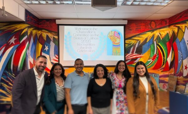 Group photo of UIC faculty, staff, and community leaders standing together in front of a colorful mural during a Latine community recognition event.