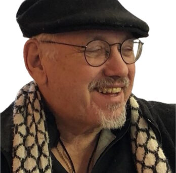 Portrait of criminology scholar John Hagedorn smiling while wearing glasses, a black cap, and a patterned scarf. 