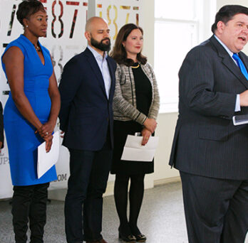 Man speaking at a podium during a public announcement, with several people standing behind him. 