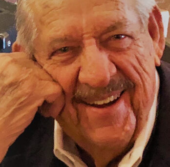 Close-up portrait of an older man smiling with his head resting on his hand. 