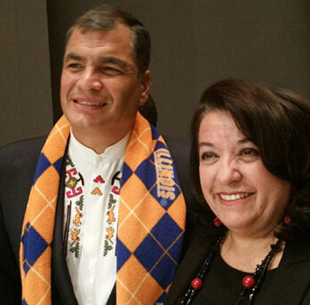Two people smiling together at an indoor event, one wearing a patterned scarf and the other standing beside him. 