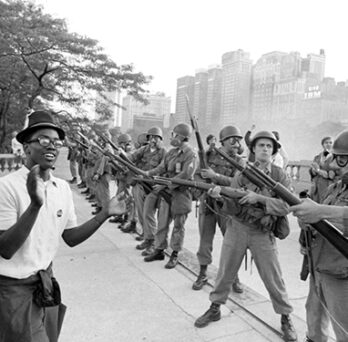 Black-and-white photo of protesters facing armed National Guard soldiers with bayonets during a street demonstration. 