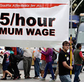 Marchers carrying a large banner reading “$15/hour minimum wage” during a public demonstration. 