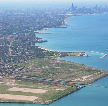 Aerial view of Chicago’s southeast lakefront, showing the former South Works site, shoreline, Lake Michigan, and downtown skyline in the distance. 
