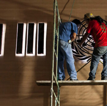Workers on scaffolding installing large “H III” letters on a wall for a Habitat III event. 