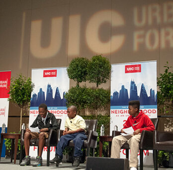 Panelists seated on stage at the UIC Urban Forum, with event signage and potted trees in the background. 