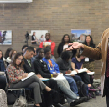 Pedro Noguera speaking to an audience during a lecture, gesturing while students and attendees sit nearby. 