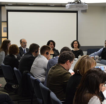 Group of civic leaders and university representatives seated around a conference table during a discussion or exchange meeting. 