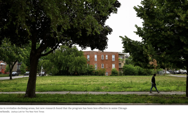 A person walks along a path through a tree-lined green space in Chicago, with a brick residential building visible in the background. Photo credit: Jamie Kelter Davis for The New York Times.