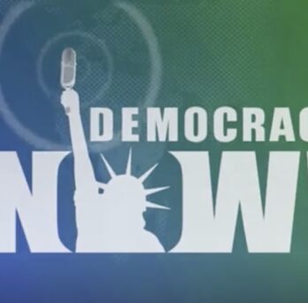 Democracy Now! logo featuring bold white lettering and a microphone held by the Statue of Liberty against a blue-green background. 