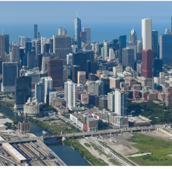 Aerial view of downtown Chicago, showing the skyline, high-rise buildings, highways, rail lines, and surrounding neighborhoods near Lake Michigan. (Curtis Waltz / aerialscapes.com)
                  