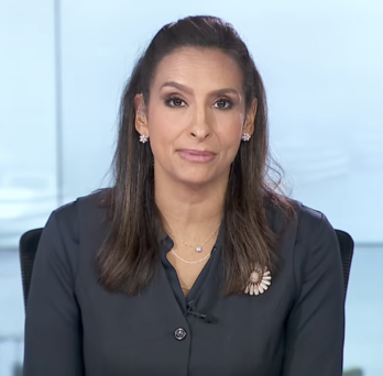 Woman seated in a studio setting, wearing a dark blazer and looking directly at the camera.