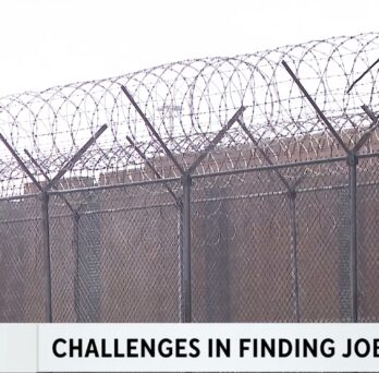 CBS News Chicago Investigators screenshot showing a correctional facility surrounded by tall chain-link fencing topped with razor wire. The lower-third news graphic reads “Challenges in Finding Jobs,” highlighting employment barriers faced by formerly incarcerated individuals.